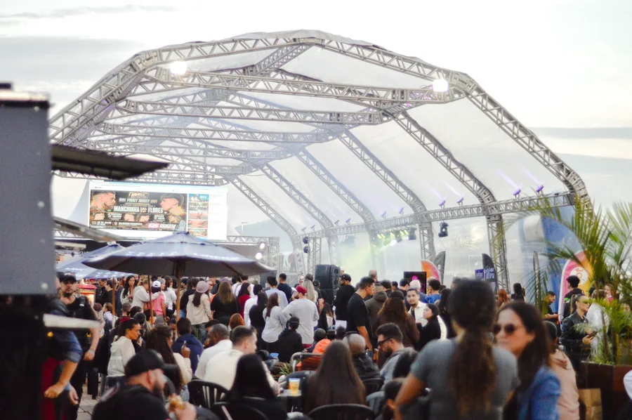 Público reunido sob a tenda, acompanhando o telão